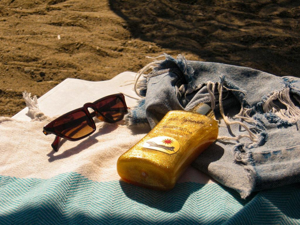 pexels photo 27292780 27292780 Sunglasses and sunscreen on a towel by the beach, capturing the essence of summer relaxation.