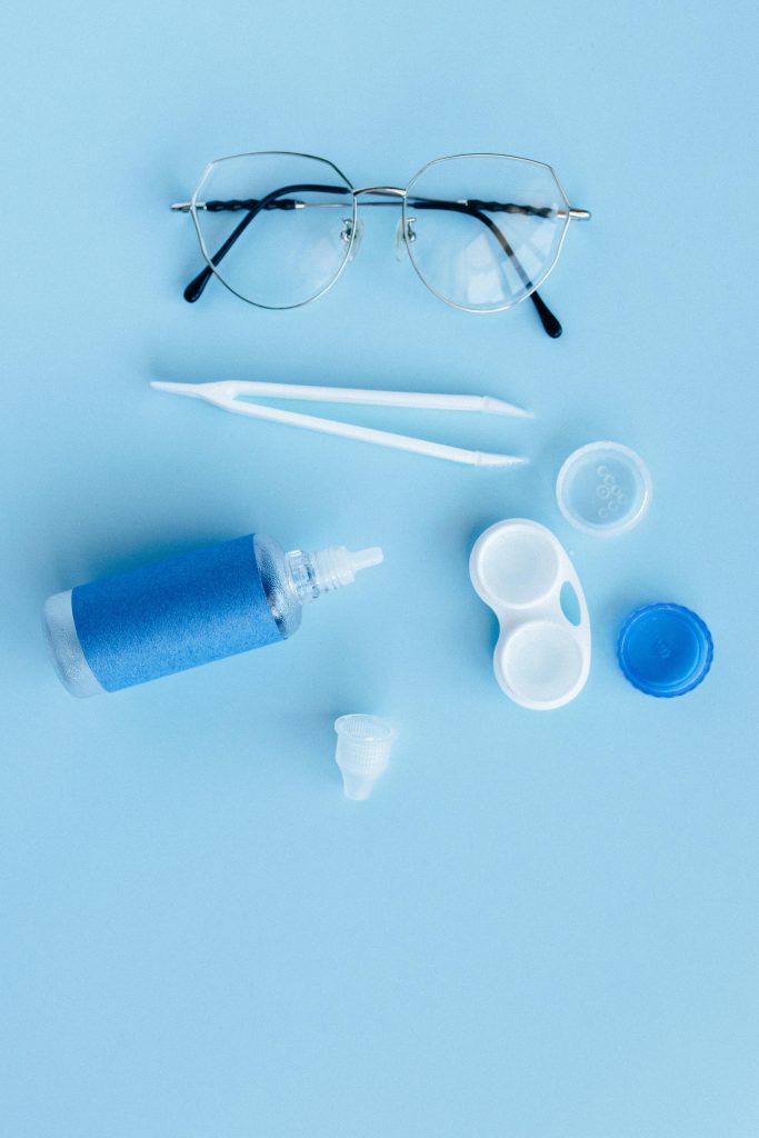 pexels photo 5843448 5843448 Flat lay of eye care essentials including glasses and contact lens solution on a blue background.