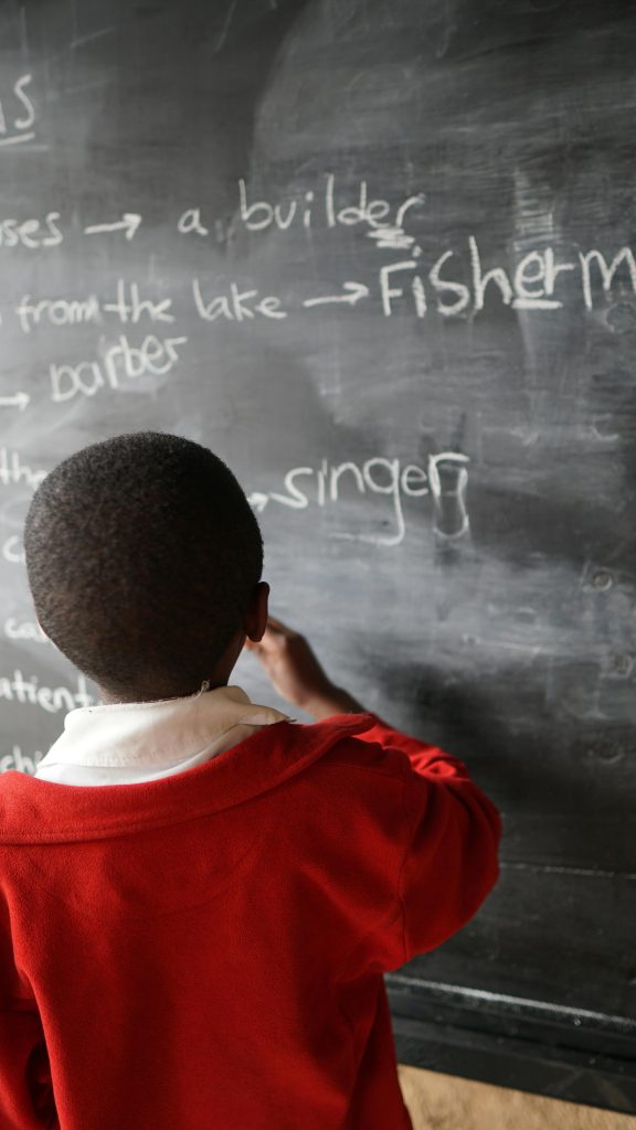 pexels photo 6827520 6827520 Young student in a red uniform writing on a blackboard, focusing on education and learning.
