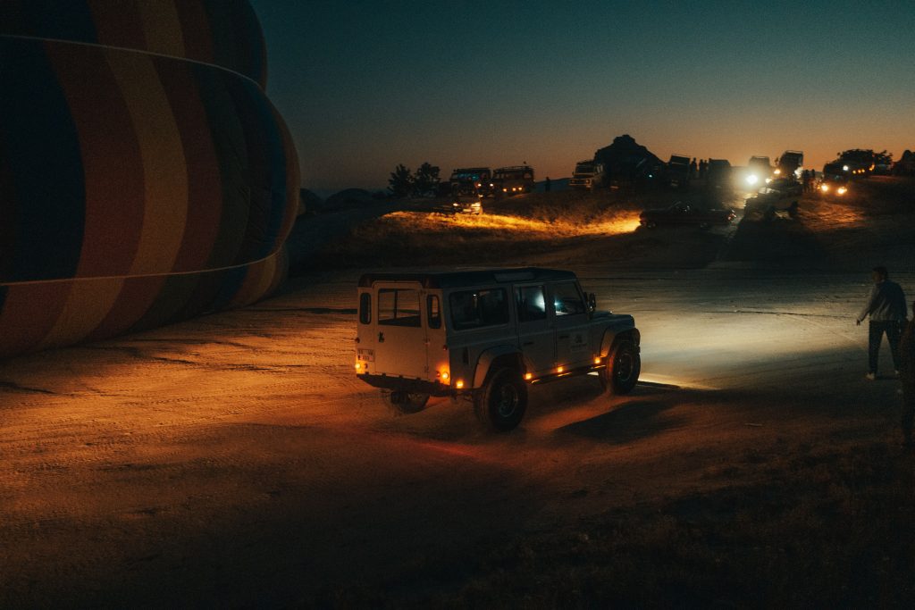 pexels photo 13524609 13524609 A white off-road vehicle parked at night beside a deflated hot air balloon, illuminated by nearby lights.